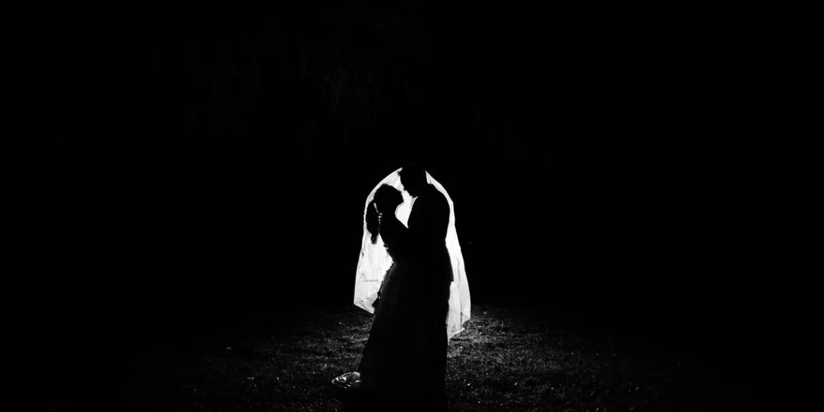 silhouette of a bride and groom at night standing underneath the brides veil the veil is illuminated
