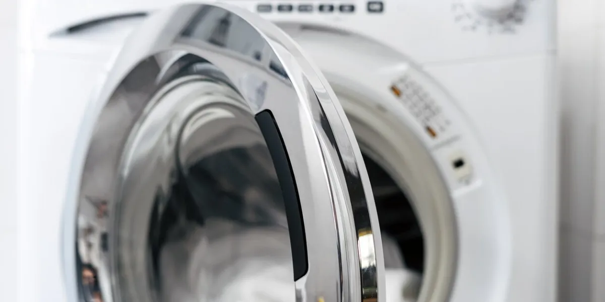 open door in automatic washing machine and clean clothes inside after laundry in apartment bathroom, modern domestic appliance