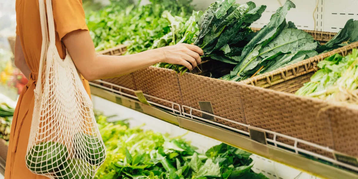 girl is holding mesh shopping bag with avocado without plastic bags at vegetable grocery shop zero waste, plastic free concept sustainable lifestyle
