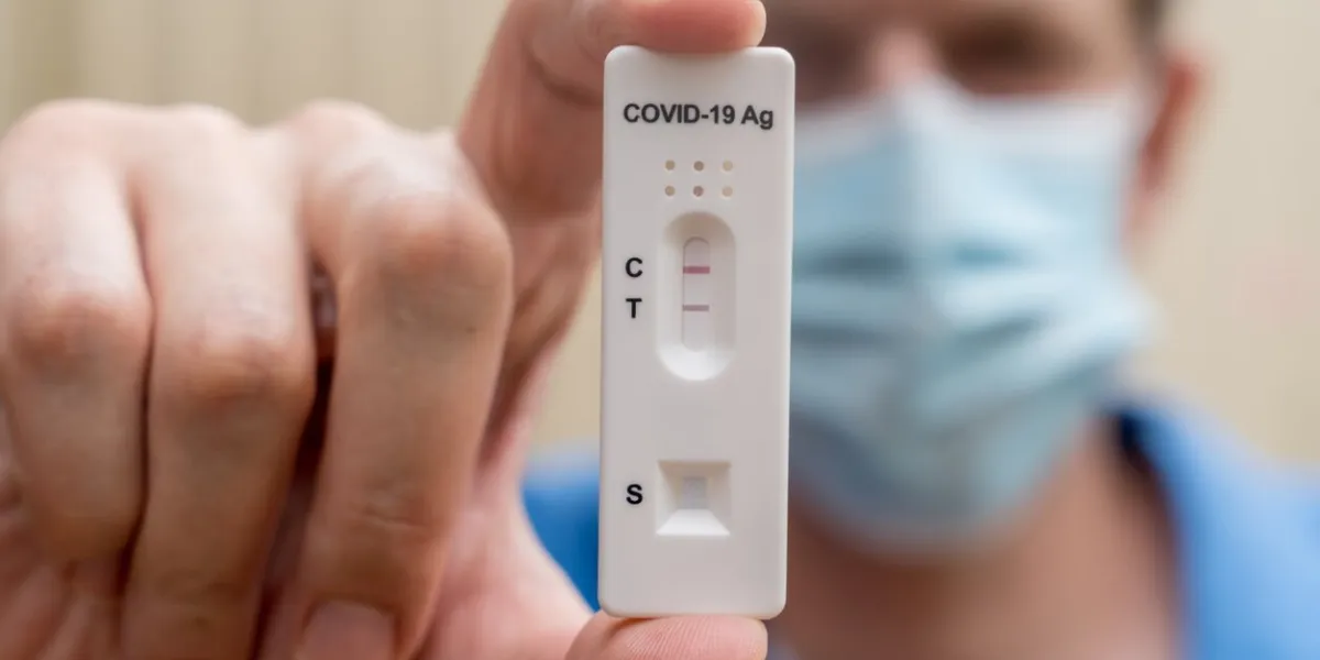 man wearing face mask holding covid-19 rapid antigen test cassette with negative result of rapid diagnostic test self-testing kit at home