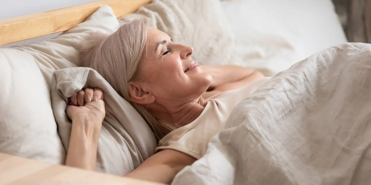 middle-aged attractive woman lying in bed on comfortable memory foam pillow fresh beige color bed clothes enjoying early morning awakened at home closed eyes dreaming visualizing perfect day concept