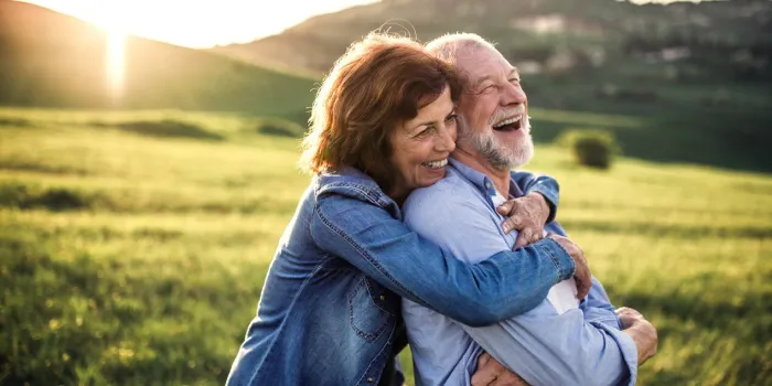 happy senior couple outside in spring nature, hugging at sunset side view