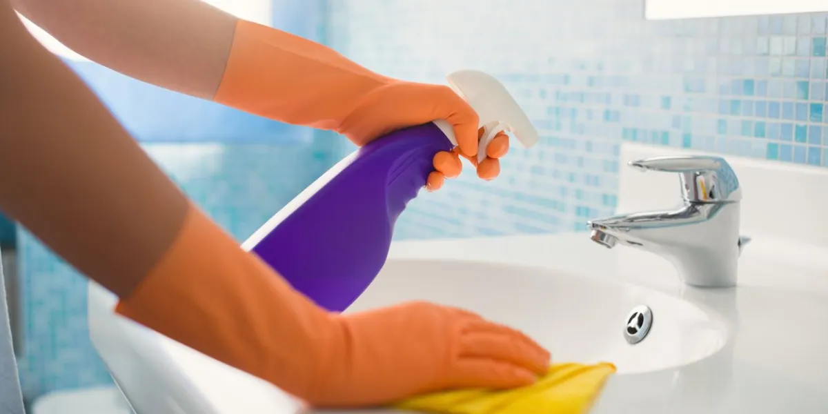 woman doing chores in bathroom at home, cleaning sink and faucet with spray detergent cropped view