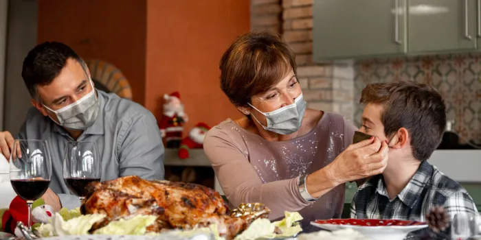 family sitting at the christmas thanksgiving table at home in the year of the coronavirus pandemic grandmother adjust the surgical mask to her grandson new rules, covid outbreak, lockdown
