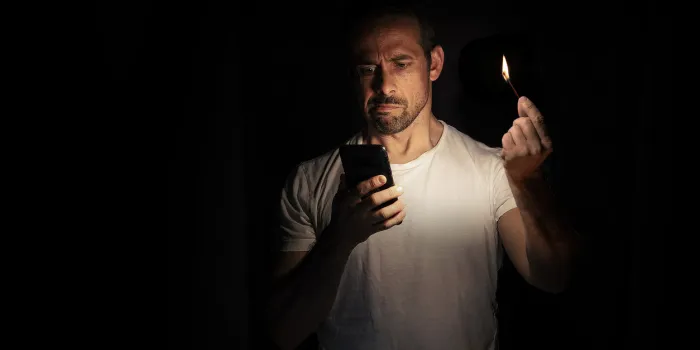 man looking at his cell phone with a match in the dark blackout concept selective focus