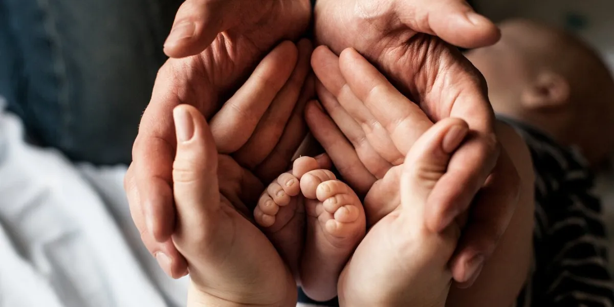 young family of mother of the father and kid mother and the father hold legs of the newborn child in the palms