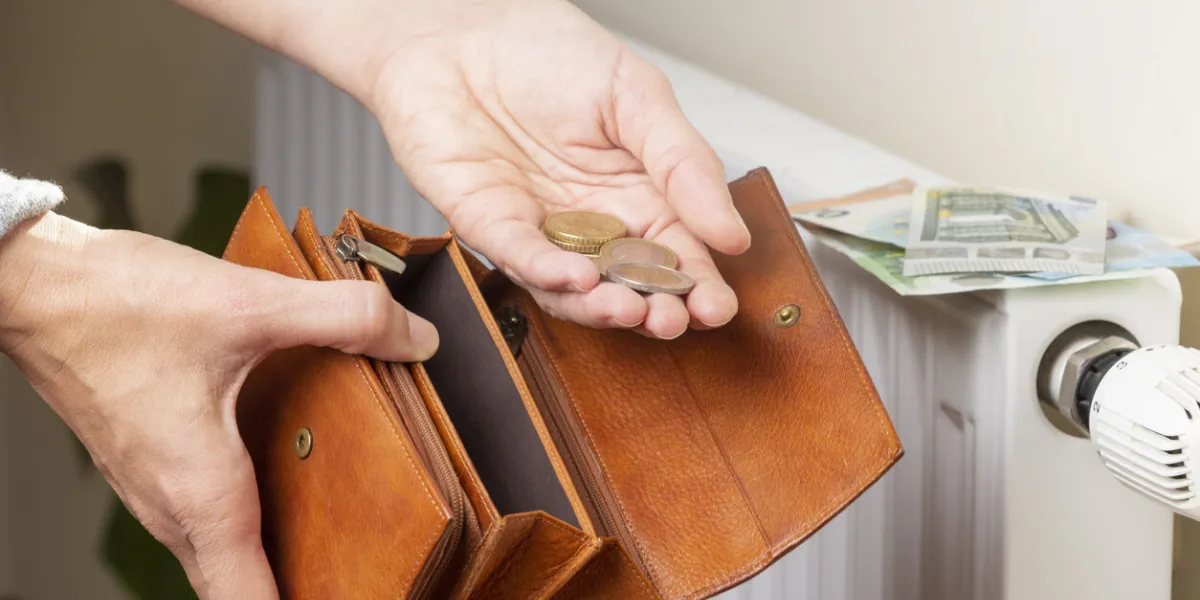 woman's hand takes euro money banknotes and coins from wallet and places on white heating radiator battery with temperature regulator expensive heating costs during cold season paying bills