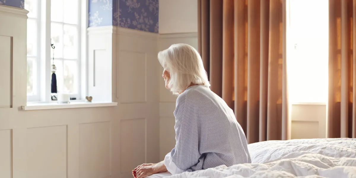 unhappy and depressed senior woman sitting on edge of bed at home