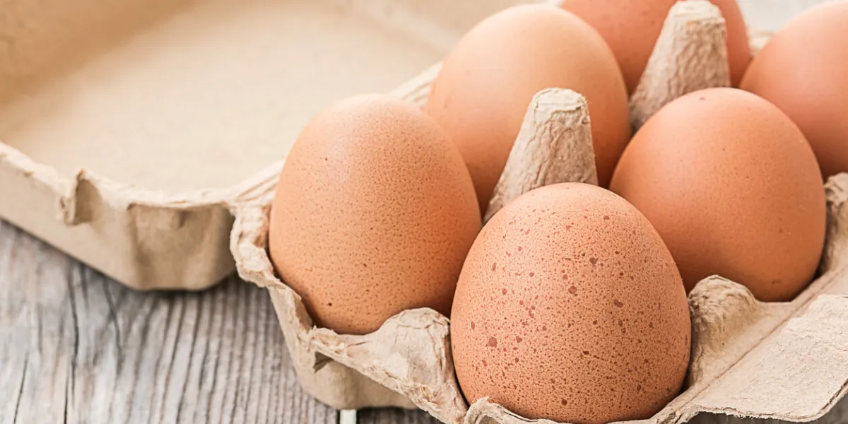 fresh brown eggs in carton on wooden table