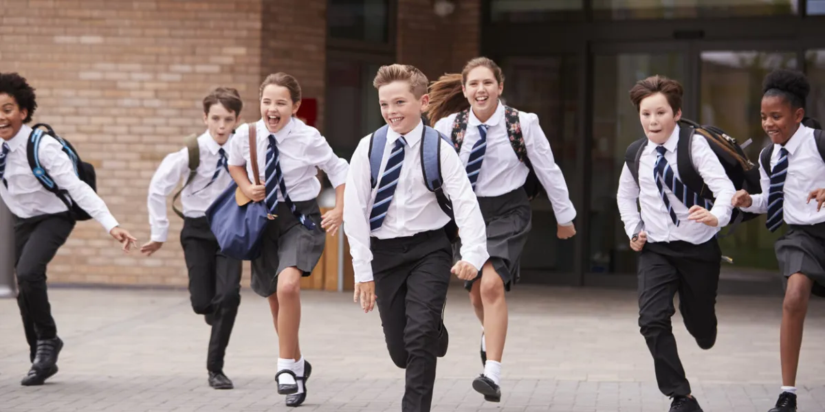 group of high school students wearing uniform running out of school buildings towards camera at the end of class