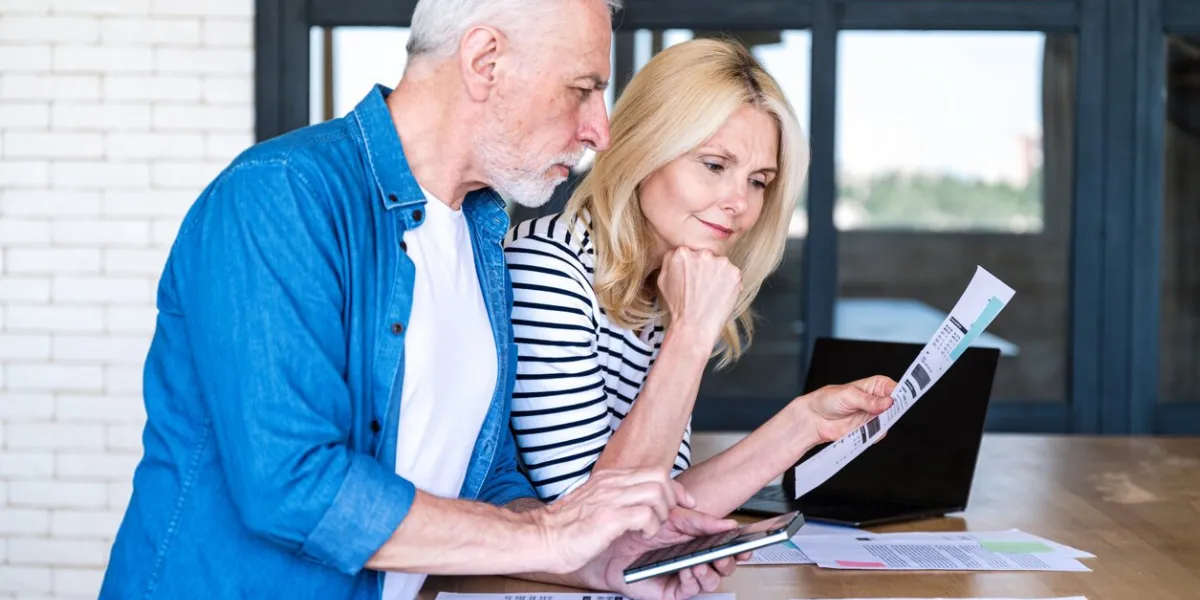 senior man in process of calculating expenses woman holding paper bills and reading, understanding documents mature husband and wife planning monthly budget together