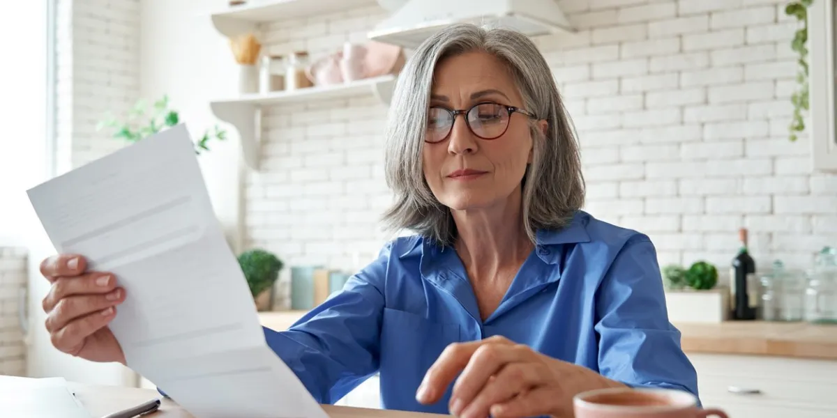 senior mature business woman holding paper bill using calculator, old lady managing account finance, calculating money budget tax, planning banking loan debt pension payment sit at home kitchen table