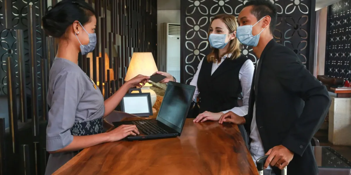 couple and receptionist at counter in hotel wearing medical masks as precaution against virus young couple on a business trip doing check-in at the hotel