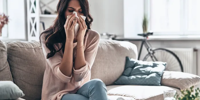 sick young woman blowing the nose using tissue paper while sitting on the sofa at home