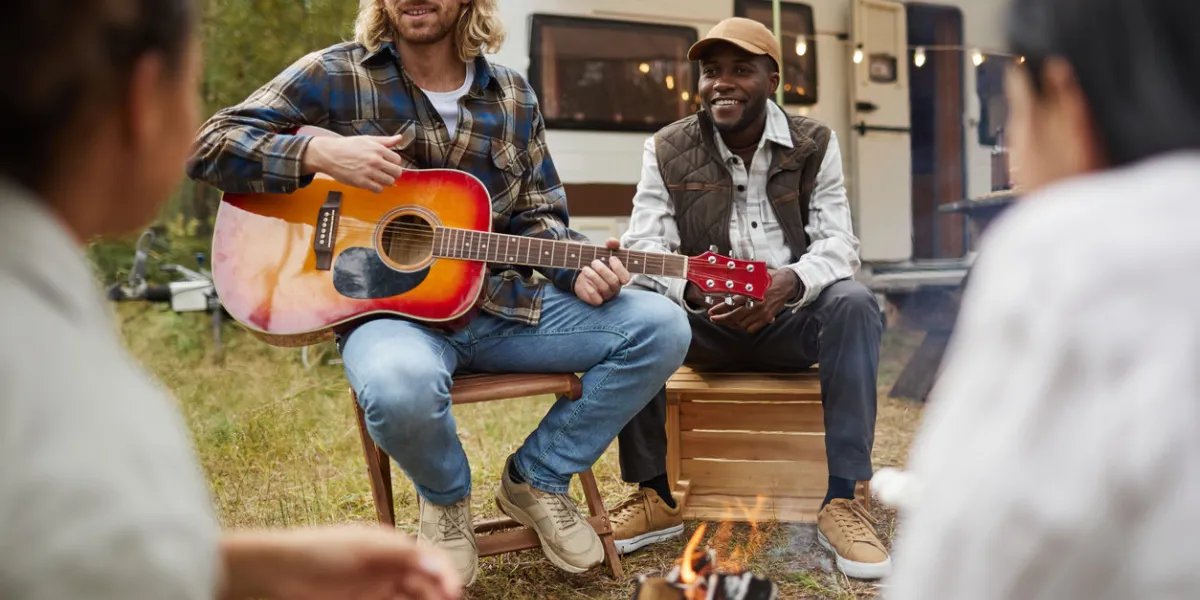 portrait of diverse group of young people playing guitar while camping with friends in forest, copy space
