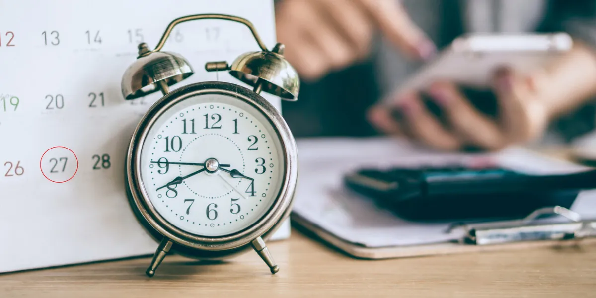 due date calendar and alarm clock with blur business woman hand calculating monthly expenses during tax season