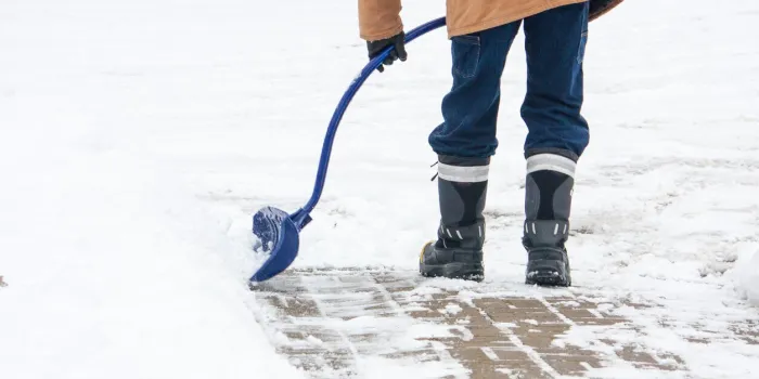 a man with a curved handled snow shovel clearing snow from a brick sidewalk in canadian winter