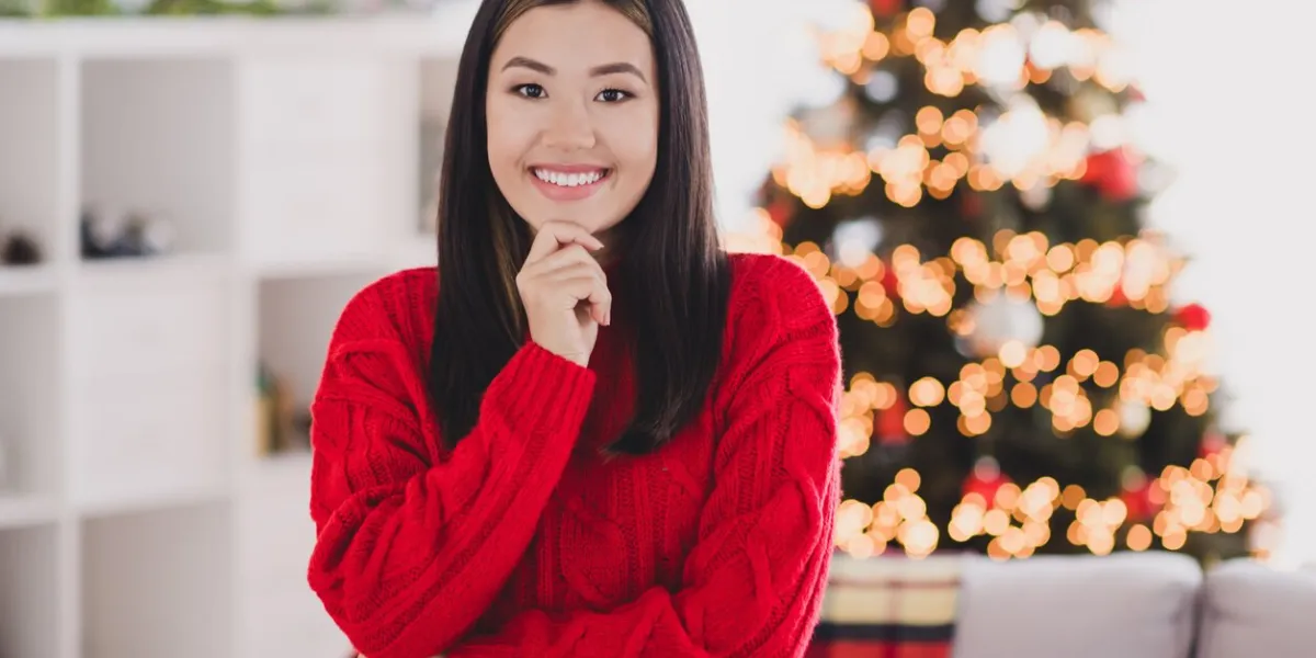 portrait of good mood adorable toothy beaming woman with straight hairdo wear red knit pullover hand on chin smiling in house indoors