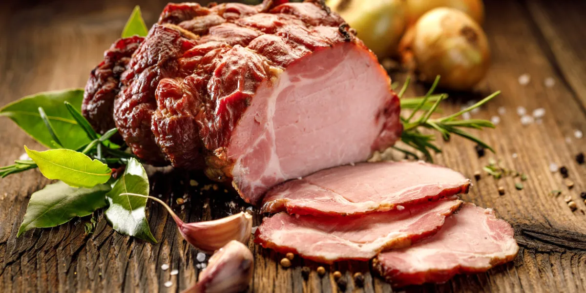 sliced smoked gammon on a wooden table with addition of fresh herbs and aromatic spices  natural product from organic farm, produced by traditional methods