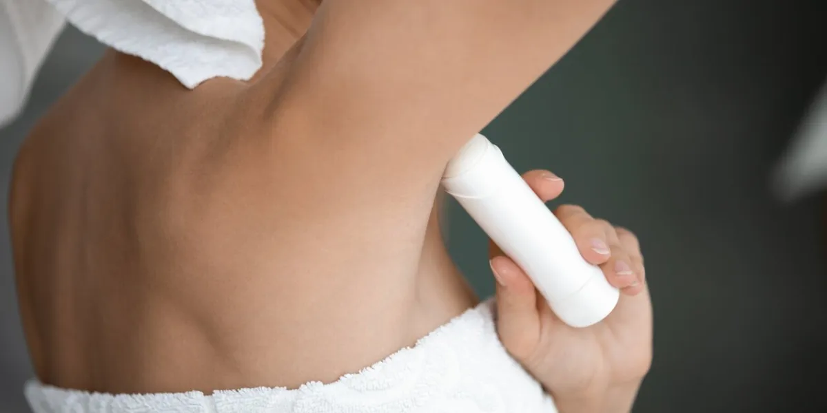 young lady wrapped in white towel raise arm apply antiperspirant in armpit, woman use underarm deodorant stick for daily hygiene everyday freshness, hyperhidrosis treatment concept close up rear view