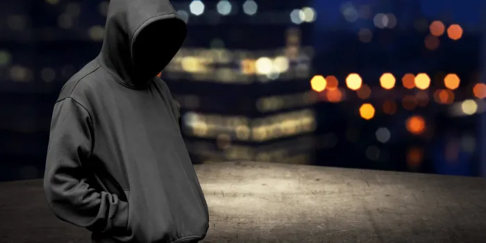 faceless man in hood on the rooftop with city background at night time