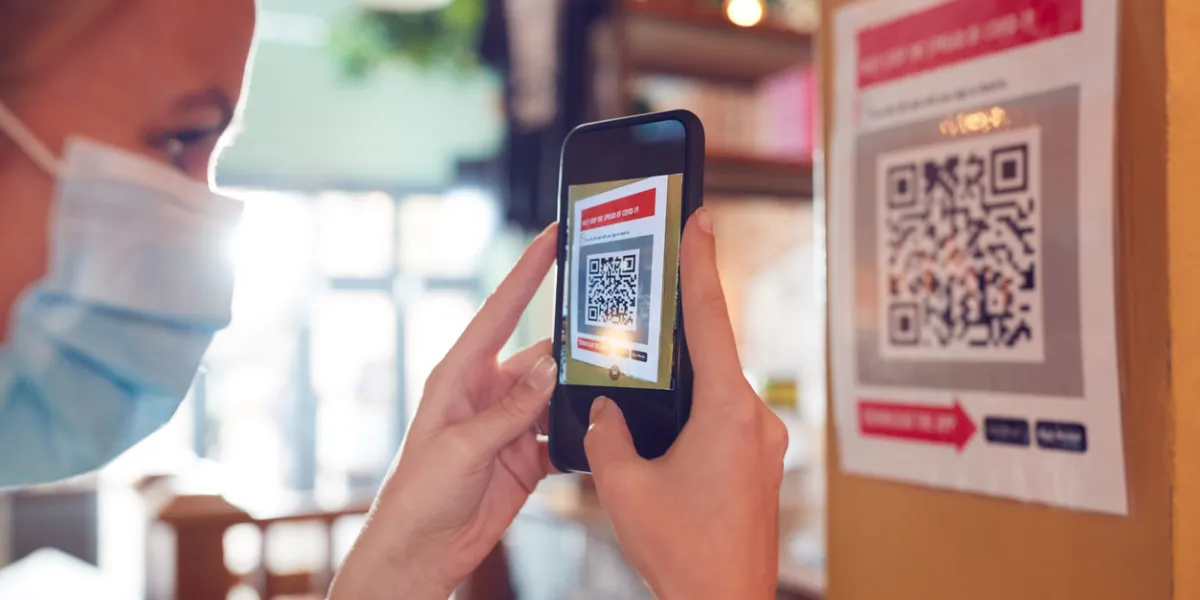 woman in mask with mobile phone checking into venue scanning qr code during health pandemic