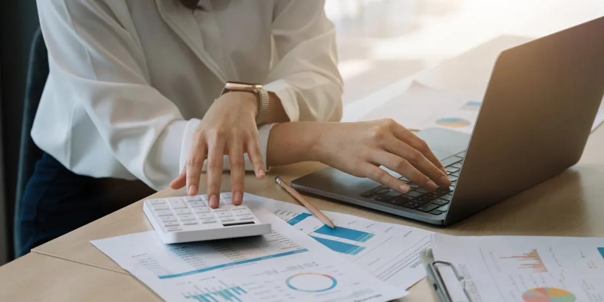 close up of businesswoman or accountant hand holding pencil working on calculator to calculate financial data report, accountancy document and laptop computer at office, business concept