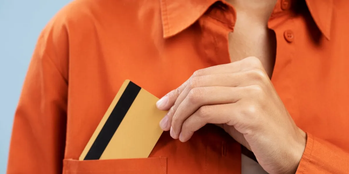 cropped view of female hand putting blank plastic credit card with copy advertising space, in the orange shirt pocket, isolated over blue background banking shopping business and purchasing concept