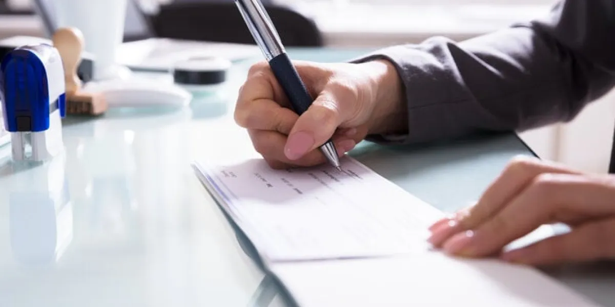 close-up of a businessperson's hand signing cheque with pen in office