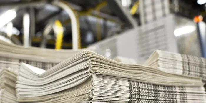 stack of freshly printed daily newspapers transported to a printing plant, in the background machines and technical equipment of a large printing plant