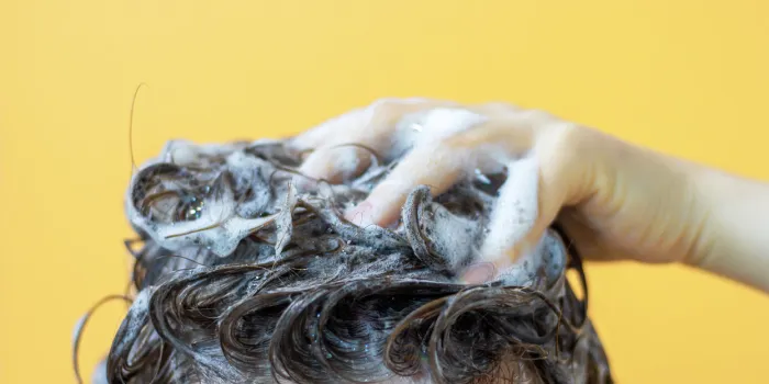 a girl washes her hair with shampoo on a yellow background, front view