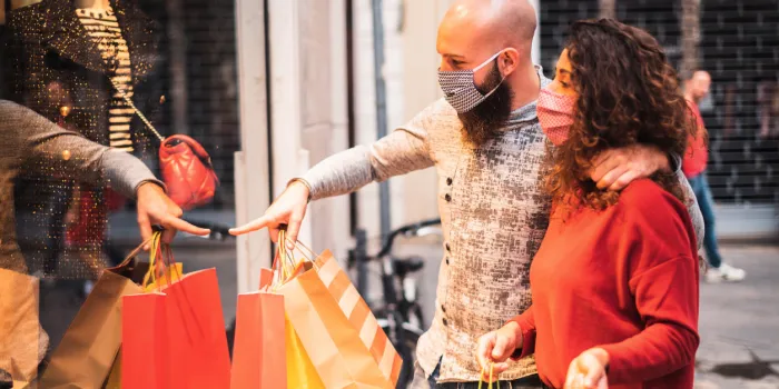 pretty young man pointing to shop window to show clothing item his likes to his girlfriend - beautiful young couple enjoying in shopping, having fun together, with the face mask - consumerism, love, dating, new normal, lifestyle concept