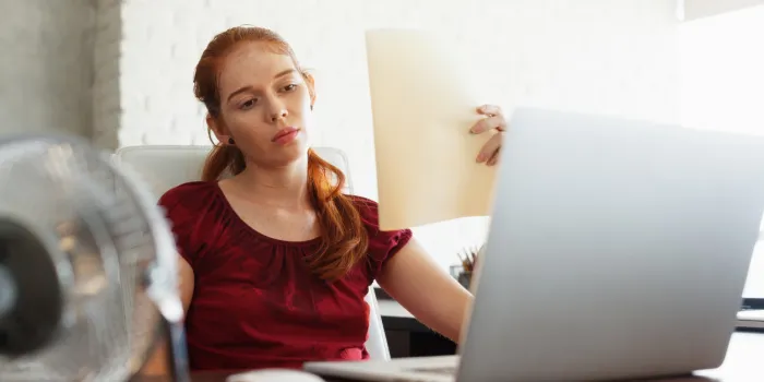portrait of young redhead woman working with computer laptop in office at summer during heatwave the temperature is hot and the hair conditioner is broken the girl sweats and feels exhausted