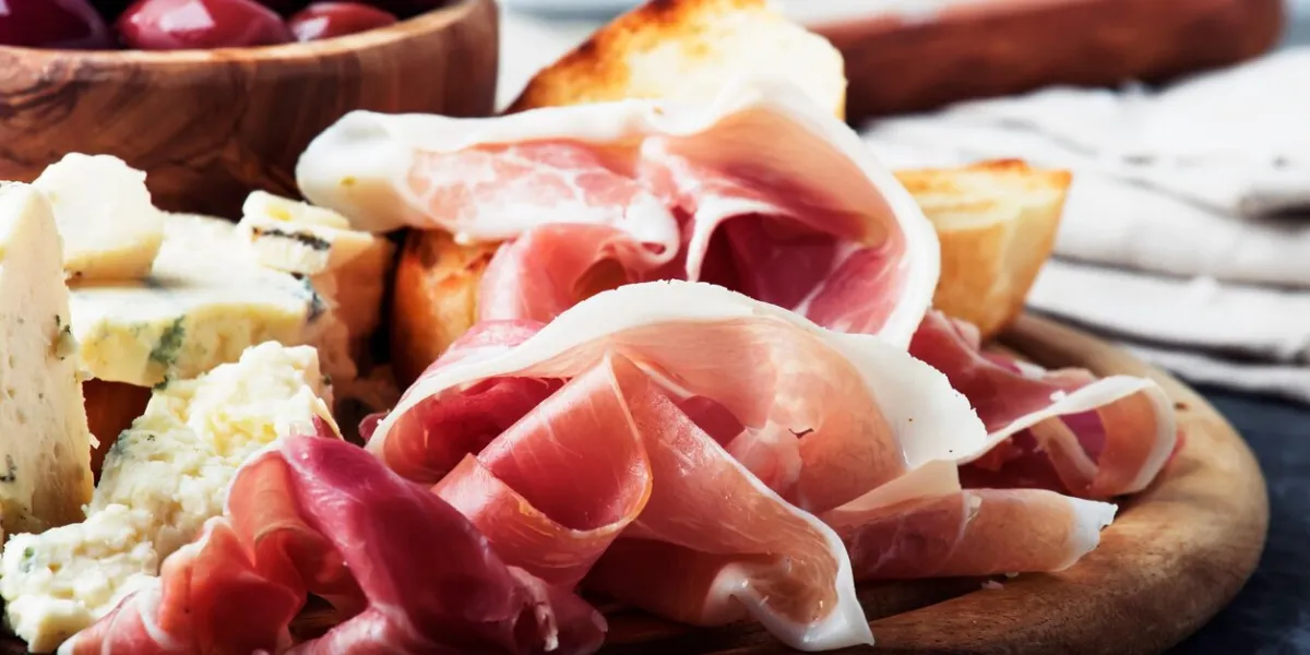 snacks or antipasti, crostini, prosciutto, blue cheese and olives, gray background, selective focus