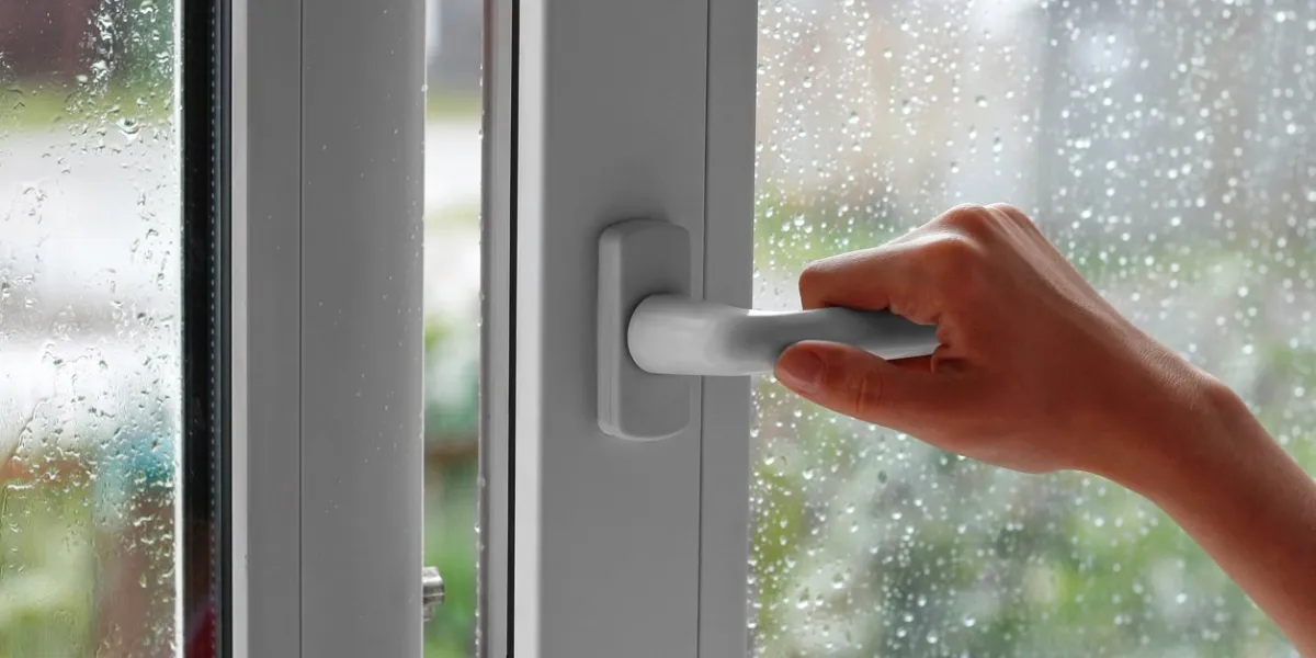 a female hand opens a window with water drops closes the window in the rainy weather closeup