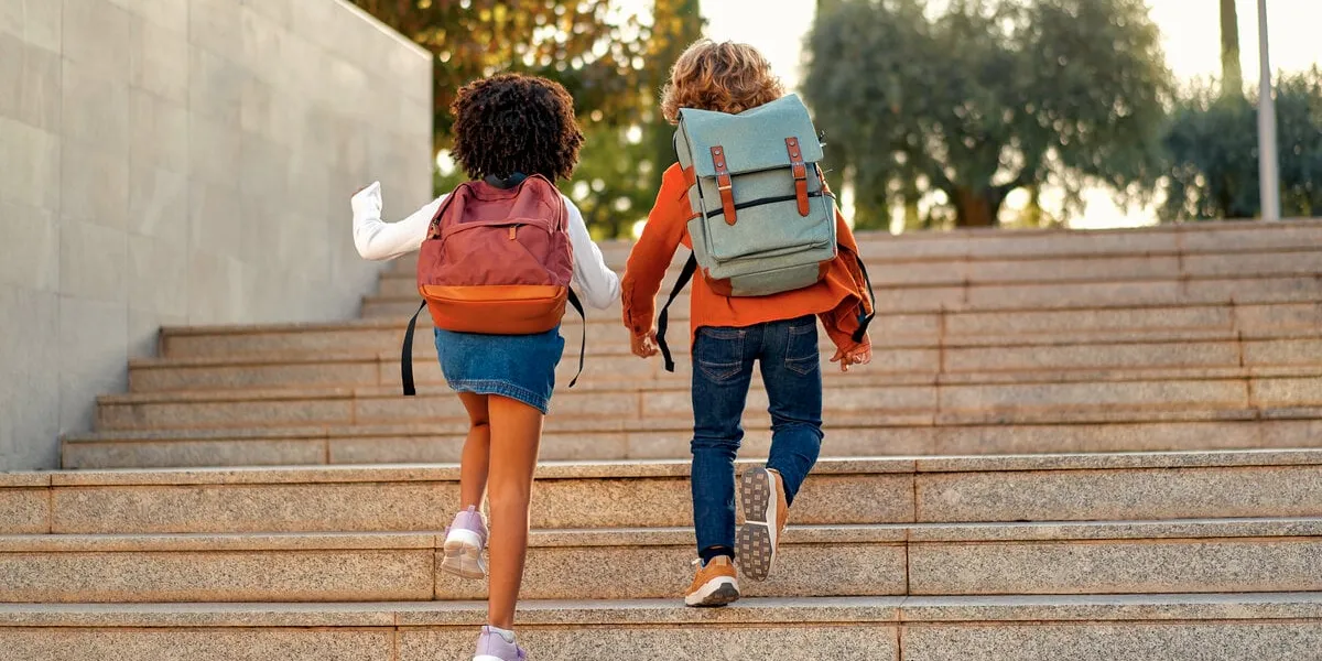 happy smart kids with school bags rush to the lessons to school running up the stairs back to school an african-american schoolgirl and her classmate walk down the street after school