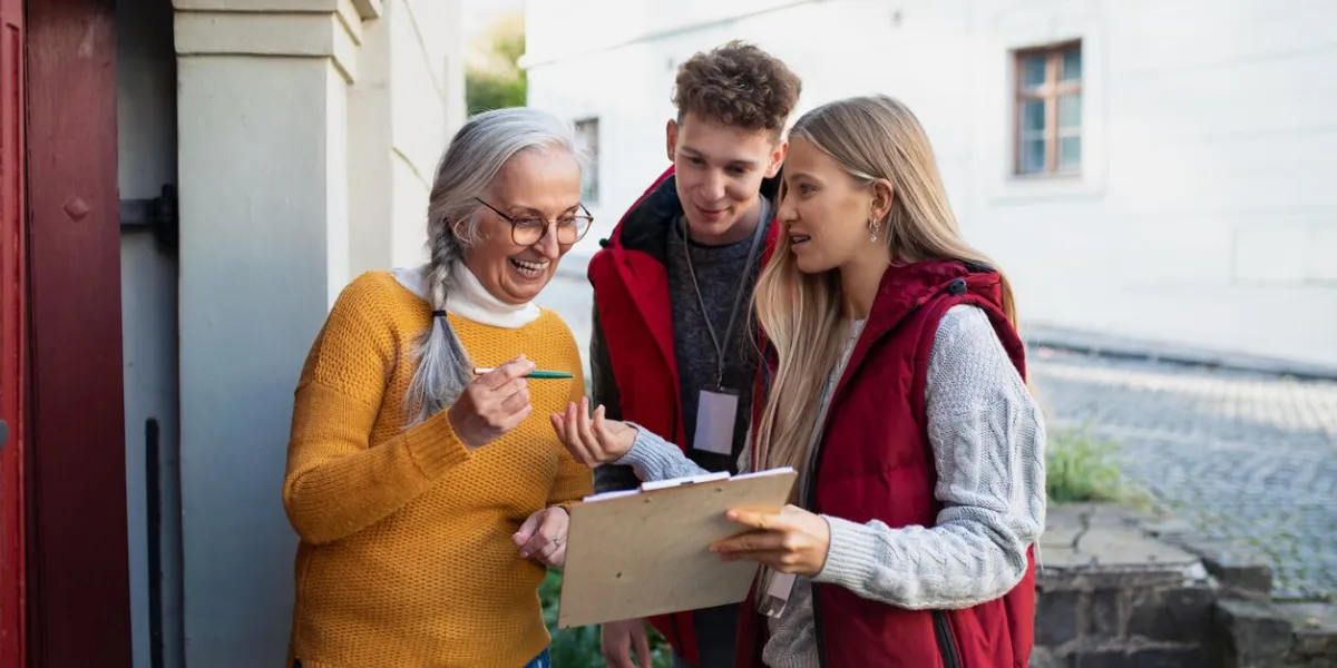 young door to door volunteers talking to senior woman and taking a survey at her front door