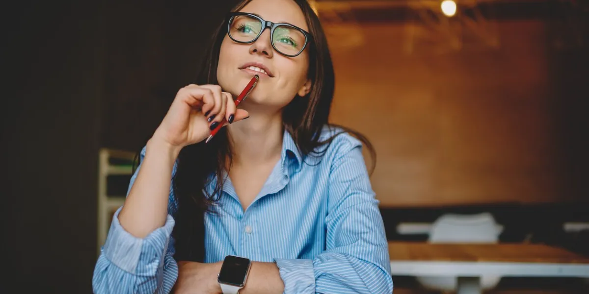 dreamy woman podring while working on journalistic publication sitting with notebook in cafe,thoughtful female student in eyewear doing homework task solving problems and analyzing information