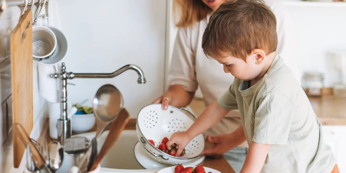 young woman mother with her toddler boy son eat srawberries in kitchen at the home