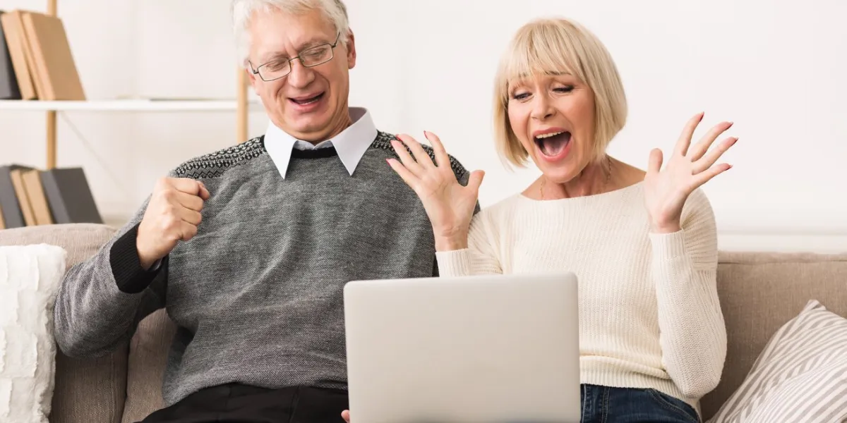 excited senior couple celebrating victory, winning online auction bid looking at laptop