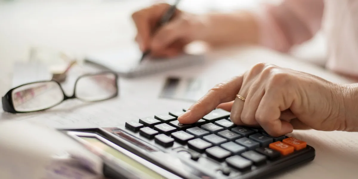 pension calculation concept, old hands counting finances on a home calculator , close- up