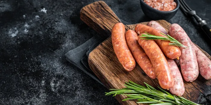 uncooked raw sausages chorizo and bratwurst with spices on wooden board black background top view copy space