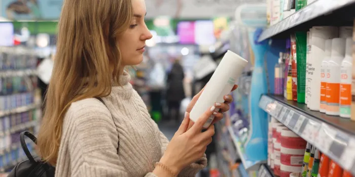 young woman picking bottles with shampoo and conditioner from shelf in cosmetics store