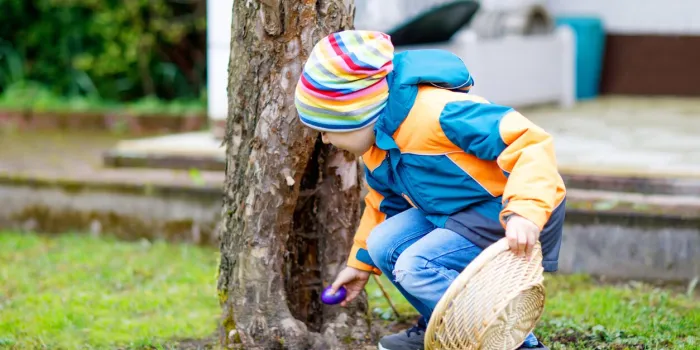 cute adorable little kid boy making an egg hunt on easter happy child searching and finding colorful eggs in domestic garden boy in spring clothes on cold day old christian and catholoc tradition