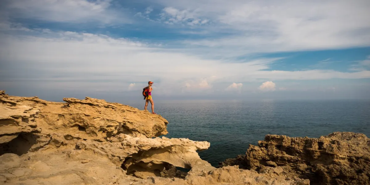 young woman hiker standing on top of the rocks and enjoying view of a blue lagoon near polis city, akamas peninsula national park, cyprus
