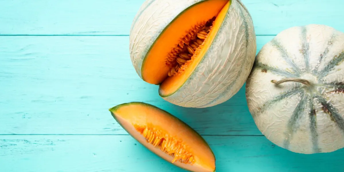 two cantaloupe melons and one slice on an aquamarine wooden planks top view
