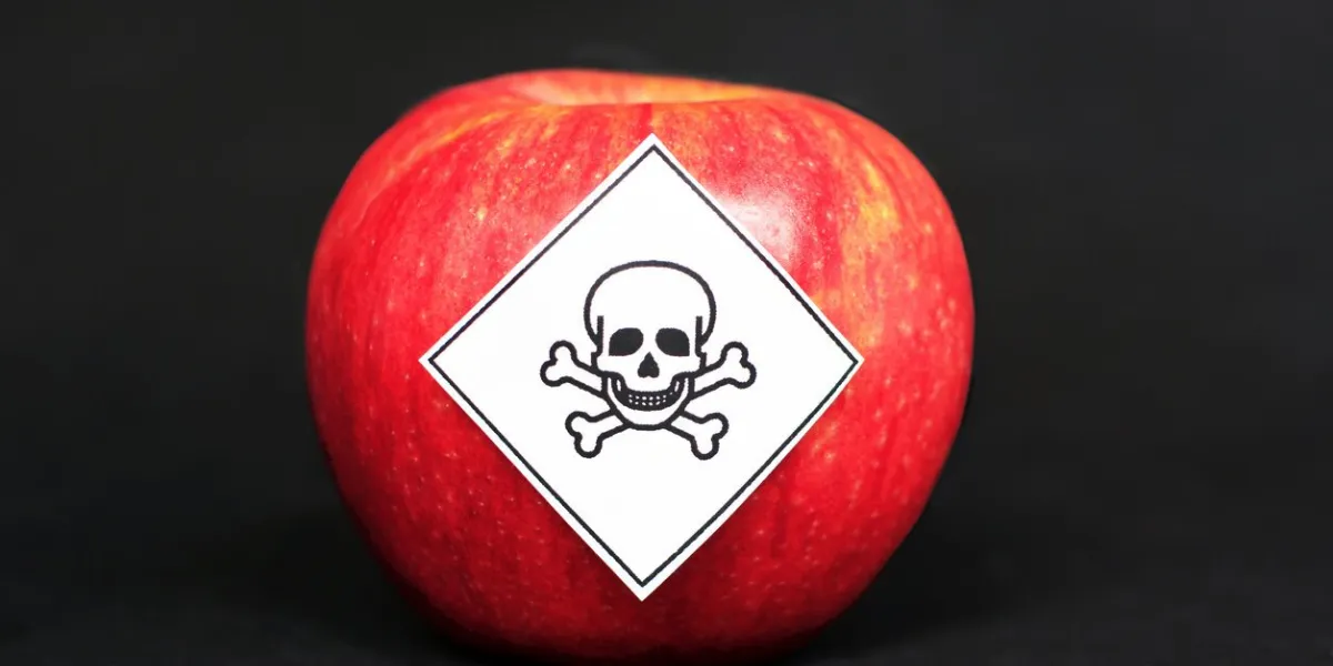 concept of pesticide residues in agricultural food products dangerous to humans, showing a red apple with poison symbol sticker on black background
