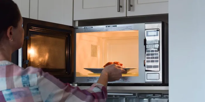 woman placing plate with food into microwave to warm up