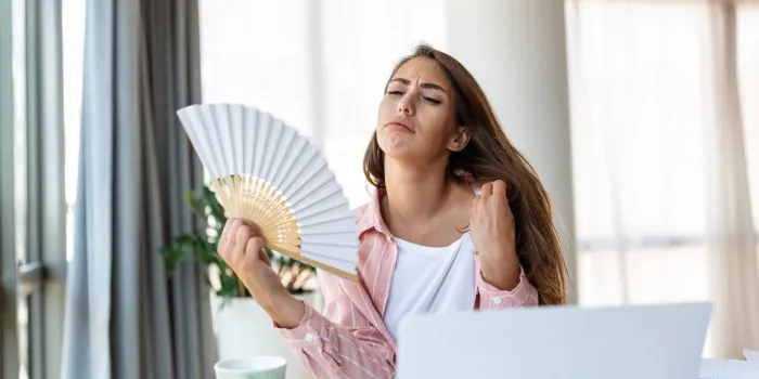 tired overheated young woman hold wave fan suffer from heat sweating indoor work on laptop at home office, annoyed woman feel uncomfortable hot summer weather problem no air conditioner concept