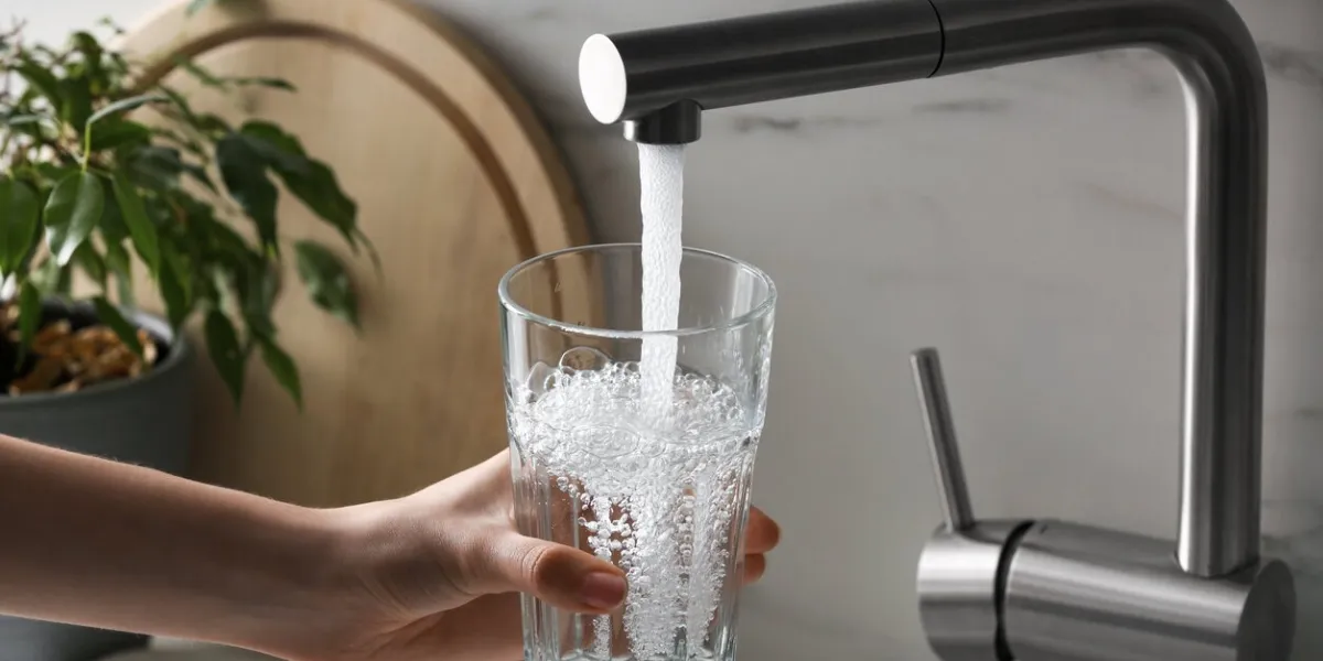 woman filling glass with tap water from faucet in kitchen, closeup